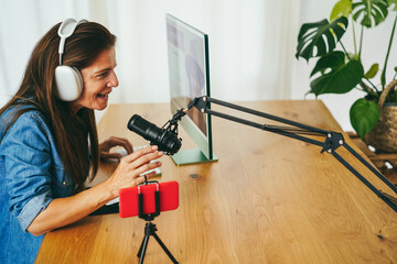Influencer woman streaming live podcast with mobile phone at home - Focus on microphone
