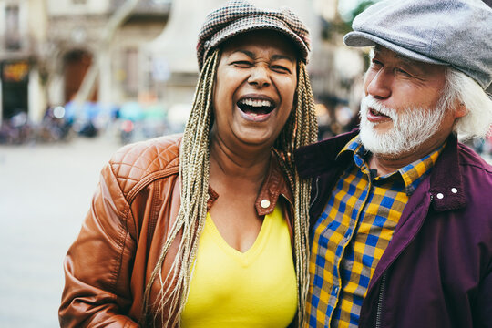 Multiracial senior couple having fun outdoor with city in background - Soft focus on man face