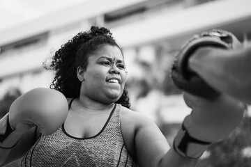 African curvy woman and personal trainer doing boxing workout session outdoor - Focus on face -...