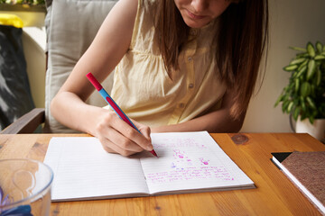 School girl writing into exercise book, doing homework
