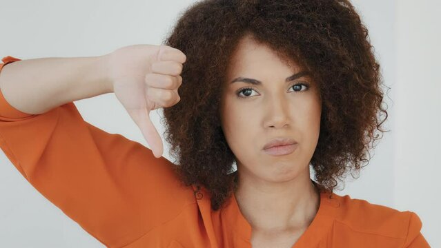 Close up angry unsatisfied African woman with curly hair displeased unhappy girl looking camera showing thumbs down rejection finger dislike negative reaction vote bad idea disapproval disappointment