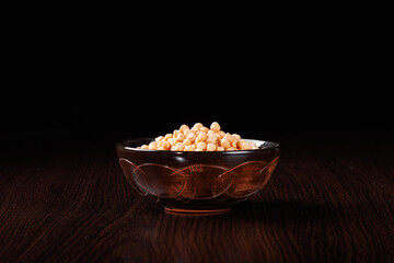 Dried chickpeas in a clay bowl on the table. Black background. Selective focus.