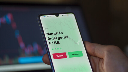 Un investisseur analyse un fonds etf march&eacute;s &eacute;mergents ftse sur un graphique. Un t&eacute;l&eacute;phone affiche le cours de l'ETF. Texte en fran&ccedil;ais francais March&eacute;s &eacute;mergents FTSE