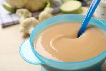 Spoon of healthy baby food over bowl on table, closeup