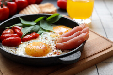 Delicious fried eggs with spinach, tomatoes and ham served on table, closeup