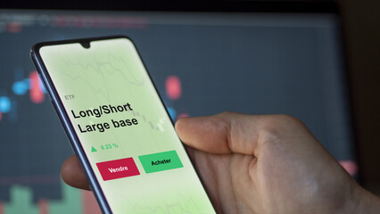Un investisseur analyse un fonds etf long/short large base sur un graphique. Un téléphone affiche le cours de l'ETF. Texte en français francais Long/Short Large base
