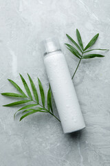 Obraz na płótnie Canvas Dry shampoo spray and green leaves on light grey table, flat lay