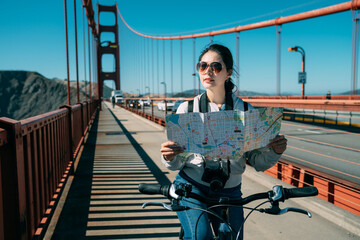 asian female traveling along on bike at golden gate bridge is searching for directions with a map...