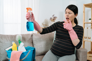 portrait asian expectant housewife with hand near mouth is feeling shocked for finding toxic chemicals while reading the label on the cleanser bottle at home.