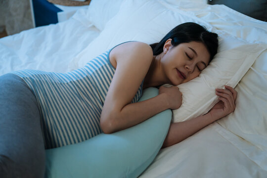 closeup pretty Asian pregnant mother is sleeping peacefully on a comfortable bed with a maternity pillow in the bedroom at night.