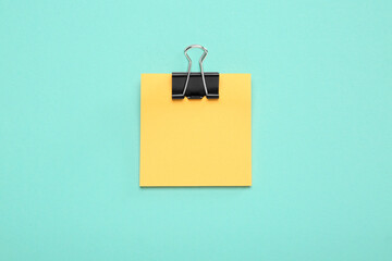 Blank orange note with black paper clamp on turquoise background, top view. Space for text