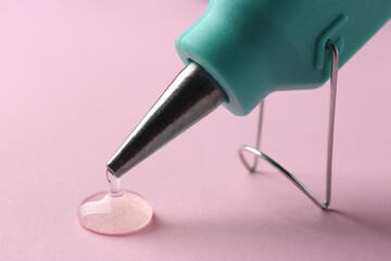 Melted glue dripping out of hot gun nozzle on pink background, closeup