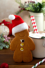 Gingerbread man cookie with Christmas red hat and hot wark drink on wooden background