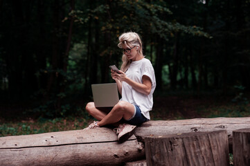 Obraz premium A girl with a laptop works while walking in the park in a cozy place, enjoys it. Online learning, freelancing and fun concept