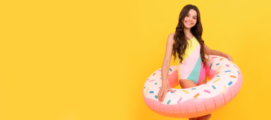 happy kid in swimming suit with doughnut inflatable ring on yellow background. Banner of summer child girl in swimsuit, studio poster header with copy space.