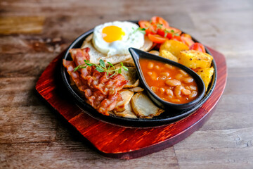Delicious English breakfast with a fries egg, beans, bacon, and roasted potatoes.