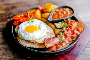 Delicious English breakfast with a fries egg, beans, bacon, and roasted potatoes.