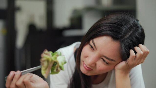 Unhappy female looking to organic greens vegetable salad in weight loss diet and wellness on table. Tired woman dislike eat bored with food healthy salad breakfast in kitchen. Diet food concept.