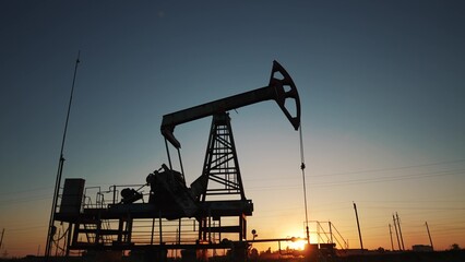 oil production. silhouette oil and gas production rig at sunset glare. oilfield business a...