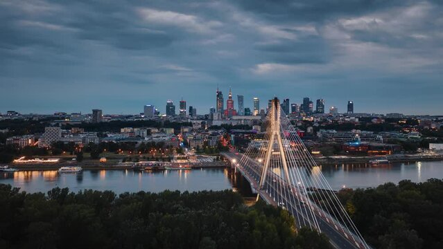 Aerial time-lapse panoramic drone shot of Warsaw cityscape. Hyperlapse suspension cable bridge over Vistula river, skyscrapers downtown urban skyline in evening. Cinematic Warsaw panorama after sunset