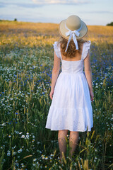 young woman in a white dress and vintage hat in a meadow with beautiful wild flowers