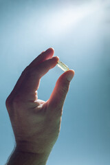 Fish oil pill in man's hand facing light and light blue background. Medical minimal creative concept. Nutritional supplements, vitamins, vitamin D, omega 3. 