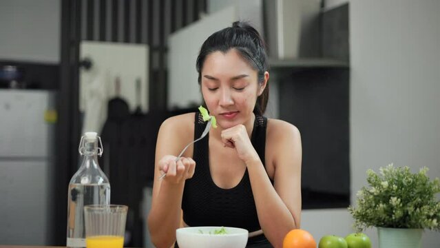 Unhappy female looking to organic greens vegetable salad in weight loss diet and wellness on table. Tired woman dislike eat bored with food healthy salad breakfast in kitchen. Diet food concept.