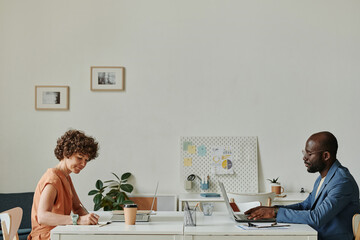 Businessman and businesswoman sitting at their workplaces opposite each other and working on...