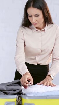 vertical video of businesswoman packing clothes in travel bag at home