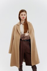 Fototapeta premium A lady with red lips in a beige coat on a white background poses for the new autumn-winter collection. Advertising for brands showrooms catalog of clothing for women