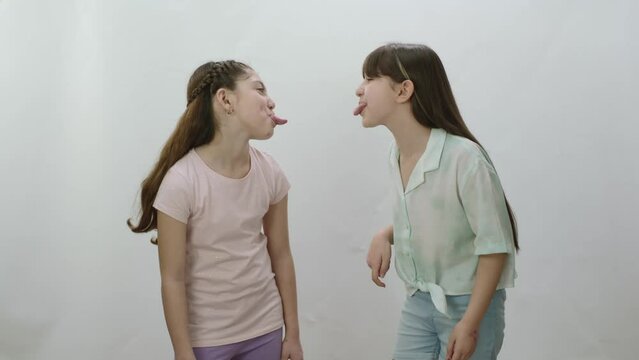 Two little girls stick out tongues at each other on white background. Those who do not love each other fight and speak out for each other. Little girls pout each other.