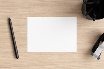 White invitation card mockup with workspace accessories on the wooden table. 5x7 ratio, similar to A6, A5.