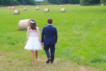 Bride and groom walking towards a green field with hay bales (Palatinate region, Germany)