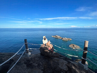 Asian tourist woman sitting on big rock at view point over blue sea background