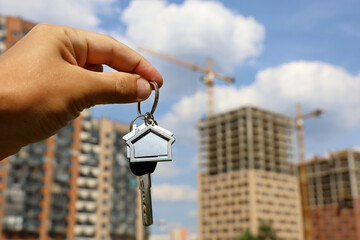 Real estate agent, keychain in shape of a house and key in male hand on background of construction...