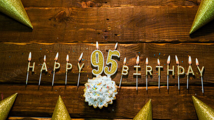 golden letters of the candle with the number happy birthday, the background of the pie with candles happy birthday on the background of brown stranded boards. Postcard Happy birthday 95