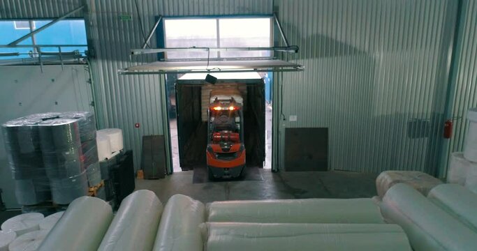 A forklift works in a warehouse. A forklift in a warehouse moves white bags. Forklift transports goods. White bags in a factory warehouse