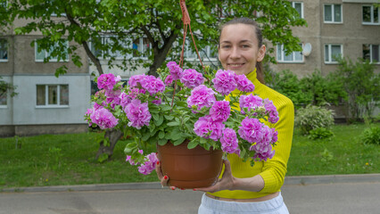 The attractive woman holding decorative petunia flower in flower pot on the street. Gardening and planting.