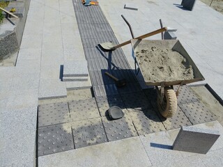 Laying gray concrete paving slabs in the courtyard of the house. Wheelbarrows loaded with cement.