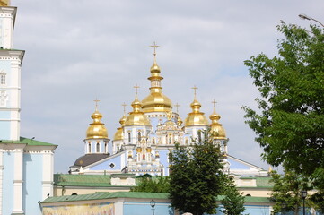 Fototapeta na wymiar Cathedral of Kiev-Pechersk Lavryna . Golden domes of the Mikhailovsky Golden-Domed Cathedral against the background of a blue sky in Kiev, Ukraine. Orthodox temple of blue color, view from the outside