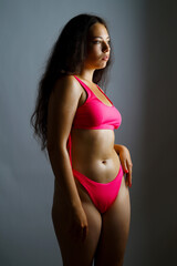 a beautiful Brazilian woman in a pink swimsuit poses on a gray background