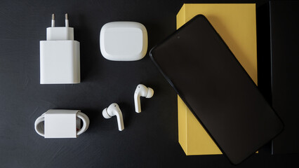 White wireless headphones, mobile phone, box, charger lie on a black background.