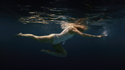A woman in a white swimsuit underwater as if in weightlessness 