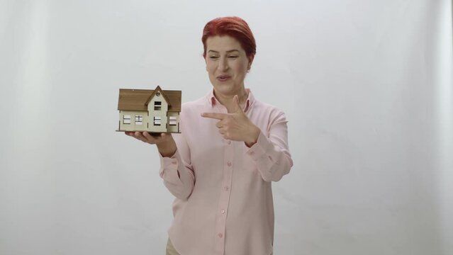 Character portrait of redhead woman holding a model of her newly bought or rented house. She examines the model of his new house, shows it to the camera and states that his house is beautiful.