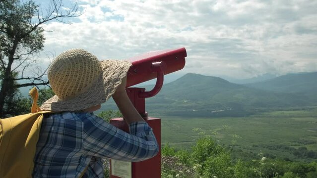 Woman looking through coin operated binoculars on mountains. Female feels freedom on summer sunny day. Cheerful woman enjoy outdoor lifestyle in holiday vacation trip