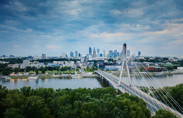 Aerial view panoramic drone shot of Warsaw city cityscape. Swietokrzyski suspension cable bridge over Vistula river, skyscrapers downtown urban skyline in evening. Warsaw panorama cloudy day
