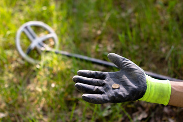 a coin found with a wireless metal detector lies on the palm of a glove. in the background, the...