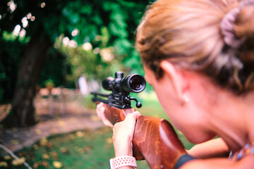 Left-handed woman practicing target shooting with an airgun in her garden.