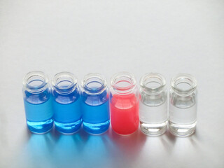 白い画用紙の上に横に並べた青色と赤色と透明な液体が入った6個のガラス瓶
