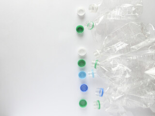 白い画用紙の右側に置いた複数の潰れたペットボトル容器とキャップとコピースペース